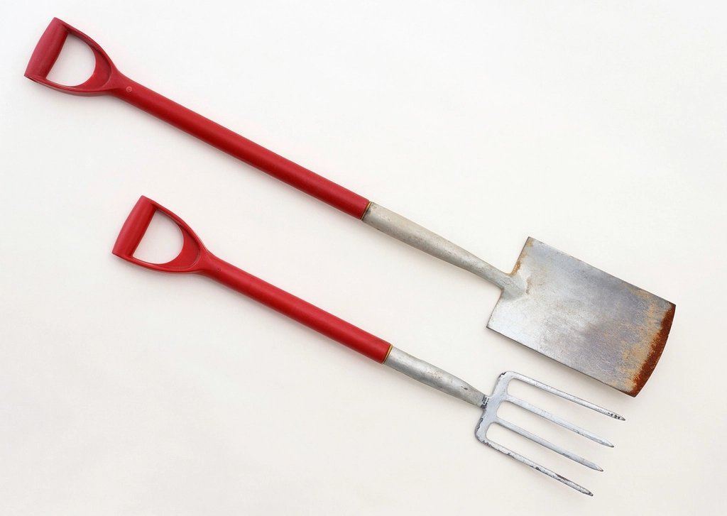 Bêche et fourche de jardin à manches rouges posées côte à côte