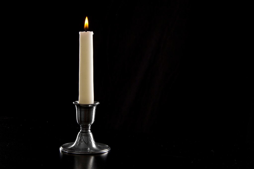 Bougeoir en étain avec une bougie blanche allumée sur fond sombre
