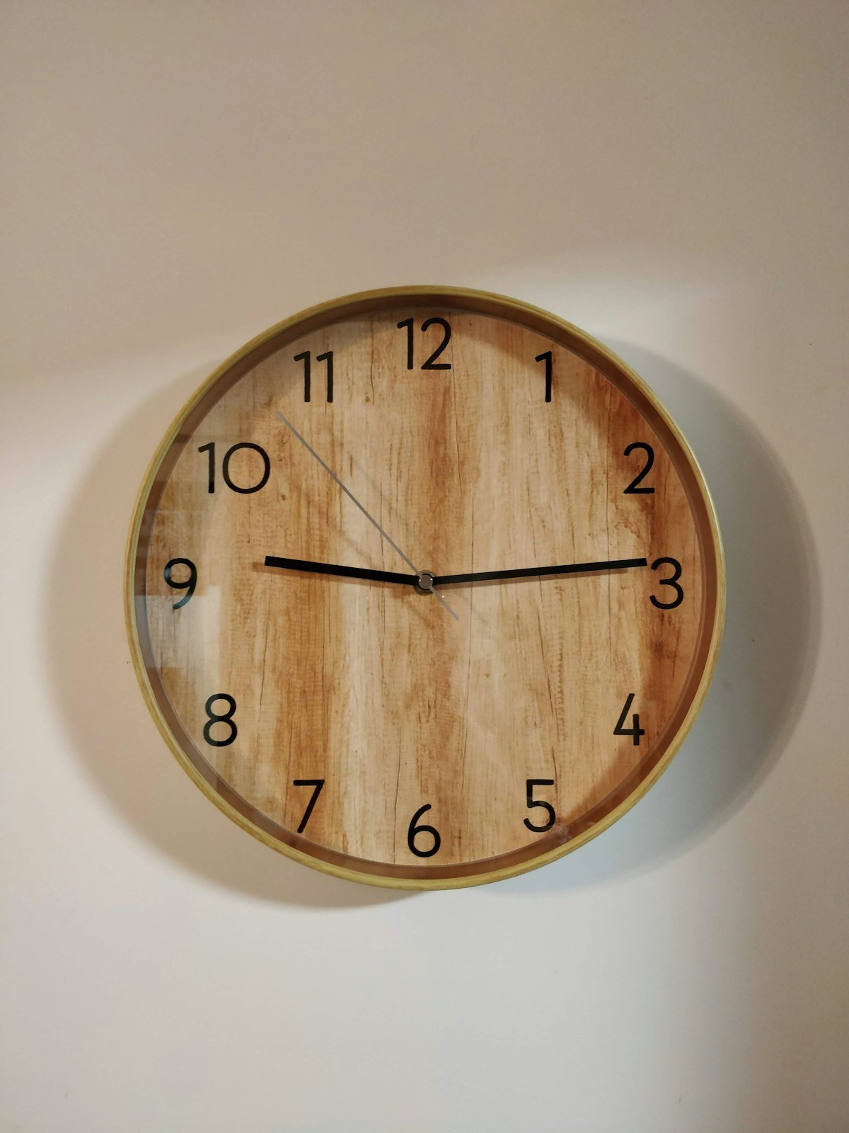 Horloge murale ronde en bois brun accrochée sur un mur clair