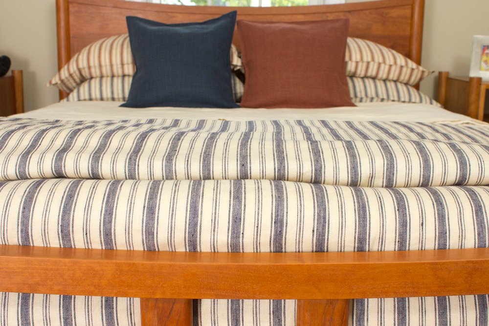 Plaid en coton rayé bleu et écru posé sur un lit avec deux coussins