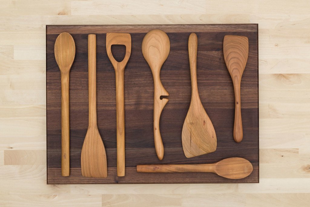 Sept ustensiles de cuisine en bois alignés sur une planche